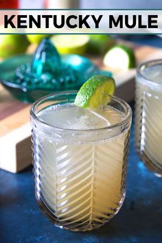 two glasses filled with lemonade and limes on a table next to a cutting board