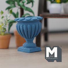 a small blue vase sitting on top of a wooden table next to potted plants