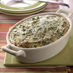 a casserole dish with spinach in it on a place mat next to plates and utensils