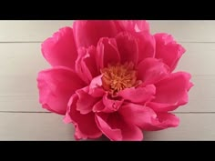 a large pink flower sitting on top of a wooden table next to a white wall