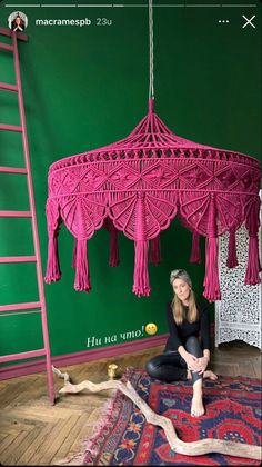 a woman sitting on top of a rug under a pink light fixture with tassels hanging from it