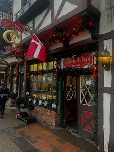 a store front with christmas decorations and lights on the windows, along with people walking down the street