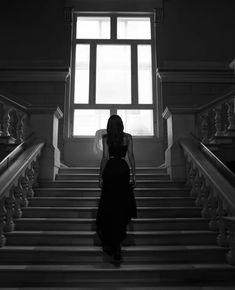 a woman is walking down some stairs in front of a window with light coming through it