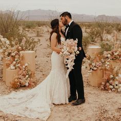 a bride and groom kissing in front of floral arrangements at their desert wedding ceremony with mountains in the background