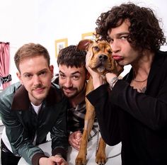 three men are posing for a photo with a dog on their lap and one man is holding the dog up to his ear