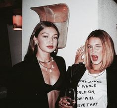 two beautiful young women standing next to each other holding wine glasses and posing for the camera