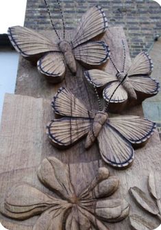 several wooden butterflies sitting on top of a piece of wood next to a brick wall