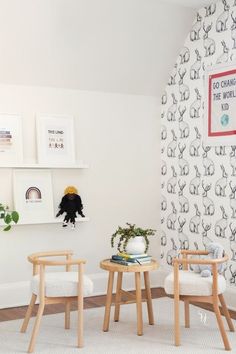 two wooden chairs sitting next to each other in front of a wall with pictures on it