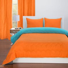 an orange and teal bed in a white bedroom with wooden floors, windows, and curtains