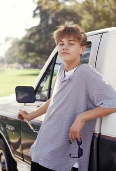 a young boy leaning against the side of a truck with his hand on the door handle