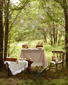 an outdoor table set up in the woods for a tea party with white and pink linens