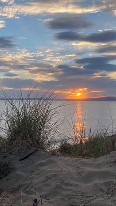 the sun is setting over the water and grass on the sand dunes at the beach