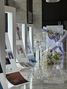 a bunch of white and purple flowers are on display in a room with columns that have pictures attached to them