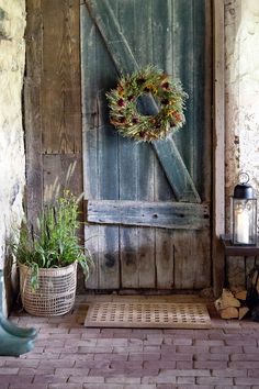 a wooden door with a wreath on it and two plants in front of it next to a brick floor