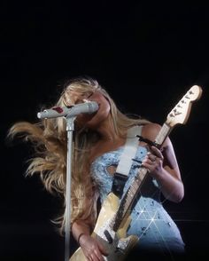 a woman holding a guitar and singing into a microphone