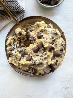 a bowl filled with cookies and chocolate chips on top of a white table next to two bowls