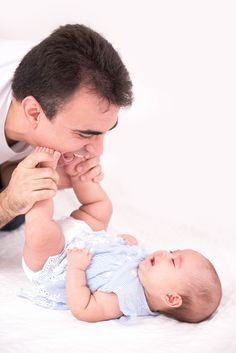 a man playing with his baby while laying on the floor in front of him and touching it's face