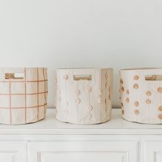 three storage baskets sitting on top of a white dresser next to each other in front of a wall