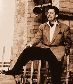 a black and white photo of a man in a suit sitting on a chair outside