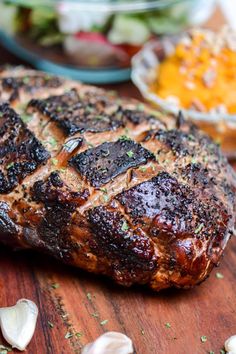 a piece of meat sitting on top of a wooden cutting board next to garlic and other food