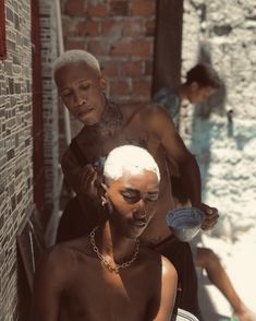 an older man getting his hair cut by another young man in front of a brick wall