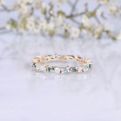 an image of a wedding ring with stones on the side and flowers in the background