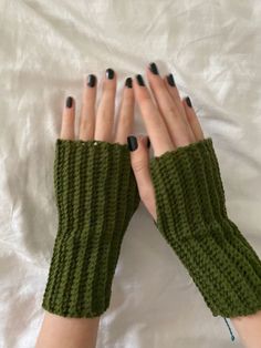 a woman's hands with black nails and green knitted arm warmers on top of a white sheet