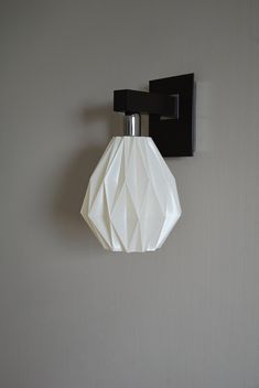 a black and white light fixture mounted on the side of a gray wall with an origami lamp hanging from it