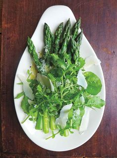 a white plate topped with asparagus and shaved parmesan on top of a wooden table