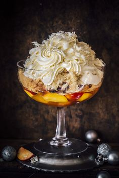 an ice cream sundae with fruit and whipped cream in a glass dish on a table