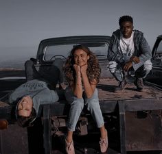 two people sitting on the back of a pick up truck in front of another person