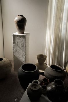 several vases and bowls are on display in a room with sheer curtains behind them