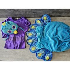 two children's clothing laying next to each other on a wooden floor, one has a blue and purple shirt with yellow eyes