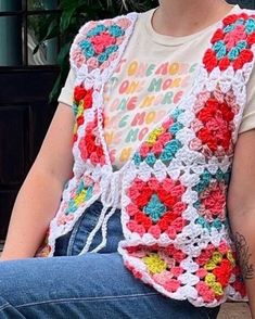 a woman sitting on a bench wearing a crocheted vest