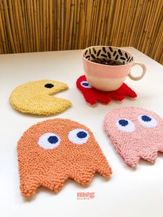 three knitted objects sitting on top of a table next to a cup and saucer