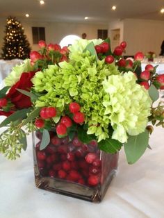 a vase filled with green and red flowers on top of a white tablecloth covered table