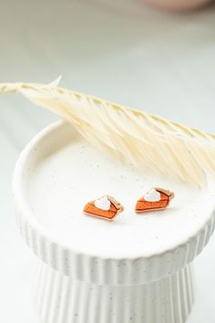 a pair of orange and white earrings sitting on top of a white plate next to a feather