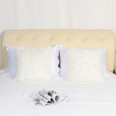 a white bed with two pillows and three rolled up newspapers on the bottom of it