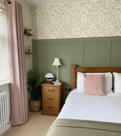 a bed sitting next to a window with pink curtains and pillows on top of it