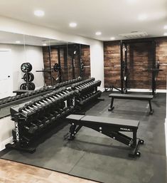 an empty gym room with benches and weight machines on the wall, in front of mirrors