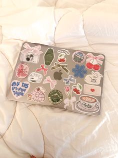 an open laptop computer sitting on top of a bed covered in white sheets and stickers