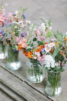 four glass vases filled with colorful flowers on top of a wooden table next to each other