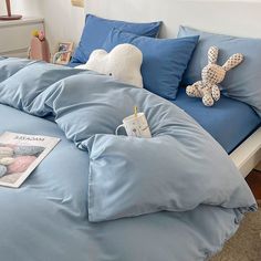 a bed with blue sheets, pillows and a stuffed animal on it's head