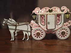 a white and pink horse drawn carriage sitting on top of a wooden table next to a lamp