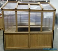 a large wooden greenhouse with glass doors on the sides and windows above it, in a warehouse