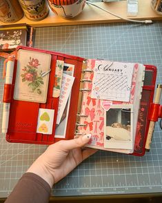 a hand holding an open planner book on top of a table next to other items