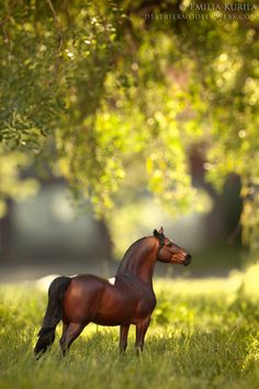 a toy horse standing in the grass near trees