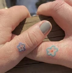 two fingers with small blue flowers on them and one has a flower tattoo on it