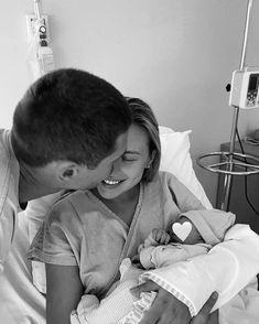 a man holding a baby in his arms while laying on a bed next to a woman