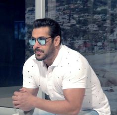 a man in white shirt and blue sunglasses sitting on window sill next to building